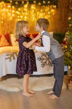 Tatlı sarışın çocuklar, kardeşler, erkek ve kız, Noel için süslü bir evde şık giyinmiş, hediyeler alıyor, mutlu oluyorlar.