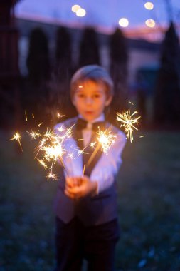 Okul çocuğu, yeni yıl arifesinde elinde maytap, arka planda havai fişek, sıradan giyinmiş, Noel ve Yeni Yıl.