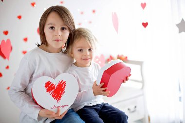 Sevimli sarışın çocuk ve ağabeyi, kalp şeklinde kutuları ve gül çiçekleri olan.