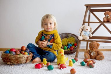 Küçük çocuk, sarışın çocuk paskalya yumurtalarıyla oynuyor. Çocuklar evde yumurta ve civcivlerle oynuyorlar.