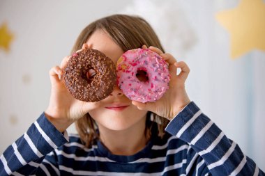 Tatlı sarışın çocuk, evde oynuyor ve donut yiyor.
