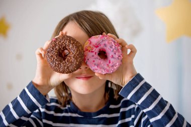 Tatlı sarışın çocuk, evde oynuyor ve donut yiyor.