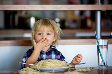 Küçük bebek, küçük çocuk, öğle yemeğinde spagetti yiyor ve oyuncak ayı arkadaş yapıyor, masanda spagetti ve domates var.