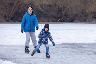 Mutlu çocuk, çocuk, sıradan giyinmiş, gün boyunca donmuş bir gölde paten kayıyor, ormanın arkasında güzel bir günbatımı, eğleniyor.