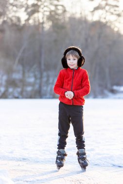 Mutlu çocuk, çocuk, sıradan giyinmiş, gün boyunca donmuş bir gölde paten kayıyor, ormanın arkasında güzel bir günbatımı, eğleniyor.