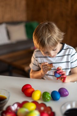 Güzel sarışın çocuk, oğlum, Paskalya için evde yumurta boyuyor ve boyuyor, bayrama hazırlanıyor.