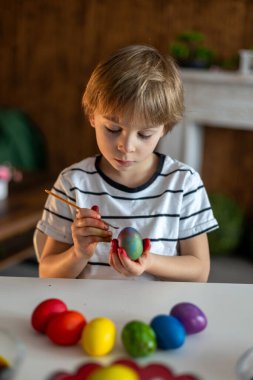 Güzel sarışın çocuk, oğlum, Paskalya için evde yumurta boyuyor ve boyuyor, bayrama hazırlanıyor.