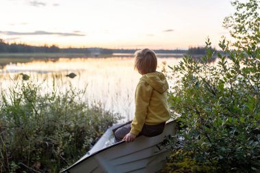Çocuklar, yazın nehirde bir teknede oynuyorlar, dürbünle doğayı izliyorlar, yaz mevsimi güneşli geçiyor.