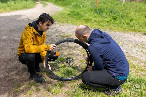 Baba ve oğul, bir aile tatilinde, bahar zamanı doğada bir bisikletin lastiğini tamir ediyorlar.