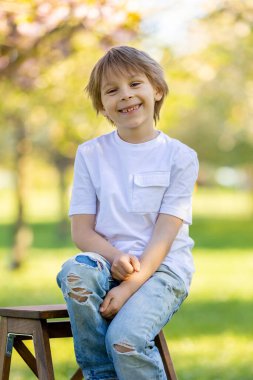 Parktaki çimenlerde oturan sevimli, şık, gülümseyen bir çocuğun portresi.