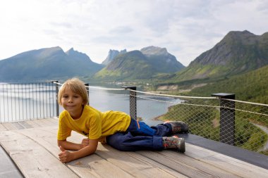 Çocuklar, 44 metre uzunluğundaki izleme platformunun kenarında durarak, Bergsfjord 'un suyuna bakarak, Kuzey Norveç' teki Senja adasının manzarasının tadını çıkarıyorlar.