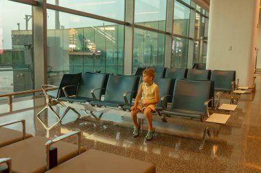 Çocuk, havaalanının penceresinden uçaklar havalanıyor ve iniyor. Tatil için uçağa binmeyi bekliyor.