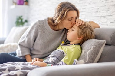 Hasta çocuk, anaokulu çocuğu, ateşi olan bir çocuk, evde köpeğiyle dinleniyor, annesi onu kontrol ediyor.