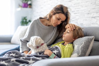 Hasta çocuk, anaokulu çocuğu, ateşi olan bir çocuk, evde köpeğiyle dinleniyor, annesi onu kontrol ediyor.
