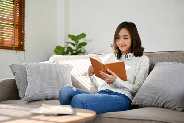迷人的年轻亚洲女人穿着休闲装 一边专心看书 一边在客厅的沙发上放松 业余爱好和休闲概念 — 图库照片