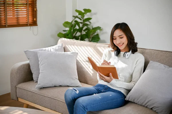迷人而快乐的年轻亚洲女人喜欢看书或小说 同时在她那狭小的客厅里舒服的沙发上休息 休闲概念 — 图库照片
