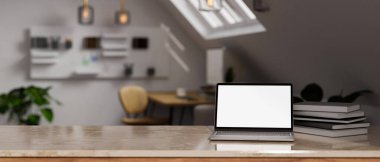 Laptop beyaz ekran maketli modern mermer masa, arka plandaki tavan arası odasındaki bulanık modern çalışma alanının üzerine kitap yığını ve kopya alanı. 3d görüntüleme, 3d illüstrasyon