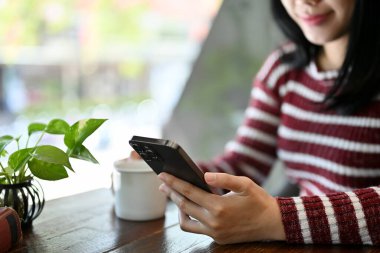 Kafede dinlenirken akıllı telefonunu kullanan güzel ve çekici bir Asyalı kadın. İnternet haberlerini okumak, sohbet etmek, sosyal medya, e-posta göndermek, online alışveriş. kırpılmış resim