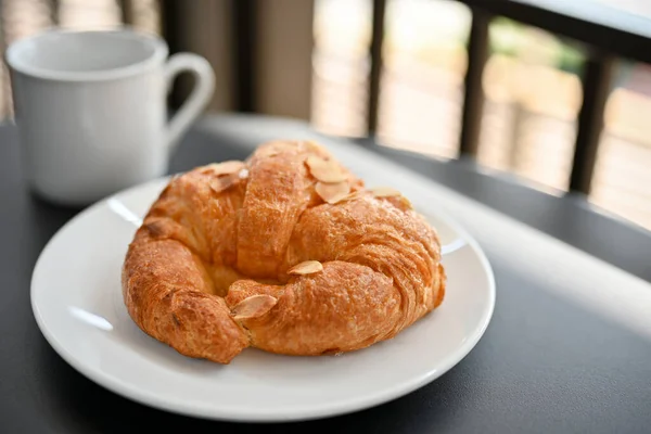 美味的新鲜法国羊角面包 白盘上有杏仁片 配上热咖啡或可可 咖啡店或面包店糕点 — 图库照片