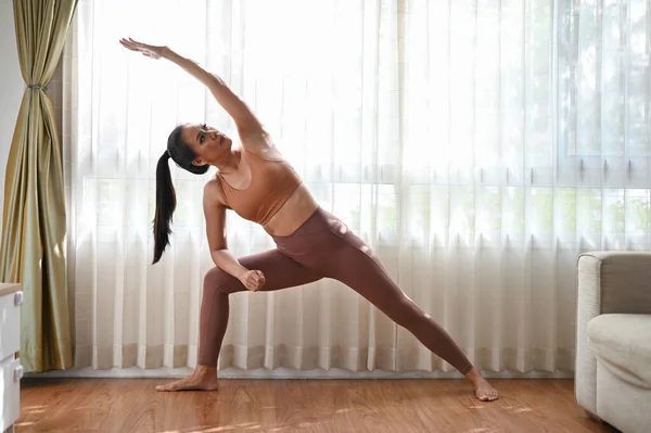 迷人迷人的亚洲女人穿着运动服 在客厅里伸展和练习瑜伽 做伸展侧角的姿势 — 图库照片