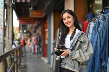 Kameraya gülümseyen ve elinde kamera olan genç bir turist portresi. 