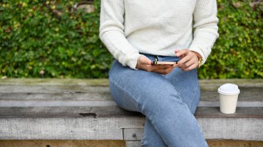 Kısa kesilmiş akıllı telefon, parkta kahve fincanıyla akıllı telefon kullanan bir kadın.