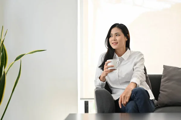 迷人的年轻亚洲女人一边喝着早茶 一边在客厅里放凉 — 图库照片