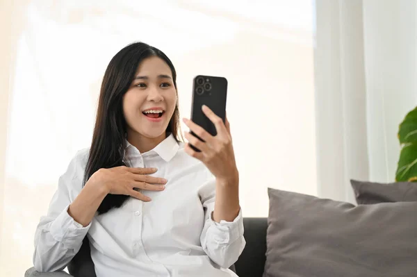 一个惊讶而快乐的年轻亚洲女人通过她的智能手机对一个意想不到的消息感到震惊 — 图库照片