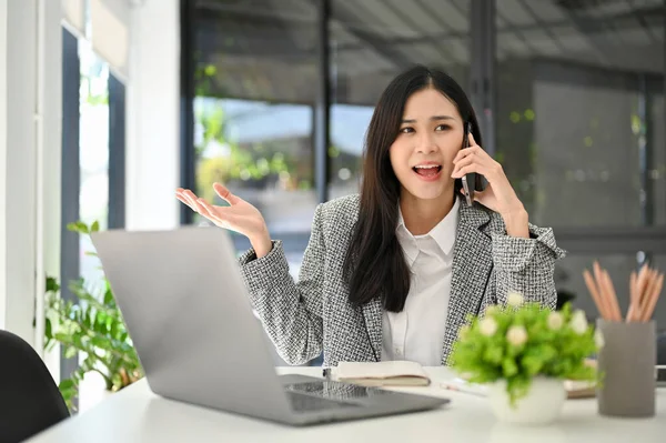 stock image Gorgeous young Asian businesswoman or female account executive talking on the phone with her client, dealing business through the call while working in her office.