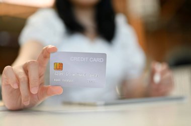 Kesilmiş atış, arka planda bulanık duran gümüş bir kredi kartı tutan bir kadın eli. Finansal, kredi kartı ödemeleri, nakitsiz toplum, bankacılık kavramı