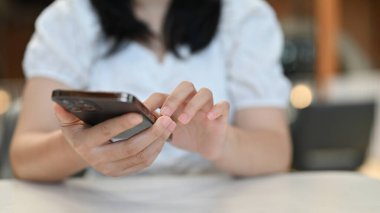 Kesilmiş atış, masasında akıllı telefonunu kullanan genç Asyalı kadın. Sohbet etmek, sosyal medyada kaymak, e-posta ve mesajlarını kontrol etmek.