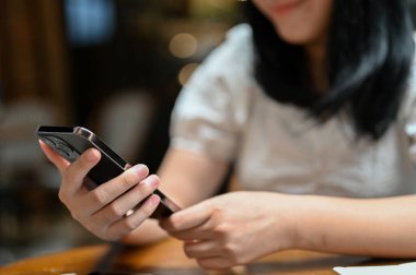 Yakın çekim, güzel ve çekici Asyalı bayan serbest ya da üniversite öğrencisi kafede dinlenirken akıllı telefonunu kullanıyor..