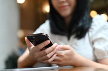 Yakın plan çekimde, kafede dinlenirken akıllı telefonunu kullanan Asyalı genç serbest çalışan ya da üniversite öğrencisi. mesajlaşma, mesajlaşma, sohbet, e-posta, sosyal medya.