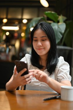 Portre, gündelik giysiler içinde güzel bir Asyalı kadın arkadaşlarıyla sohbet etmek için cep telefonunu kullanıyor..