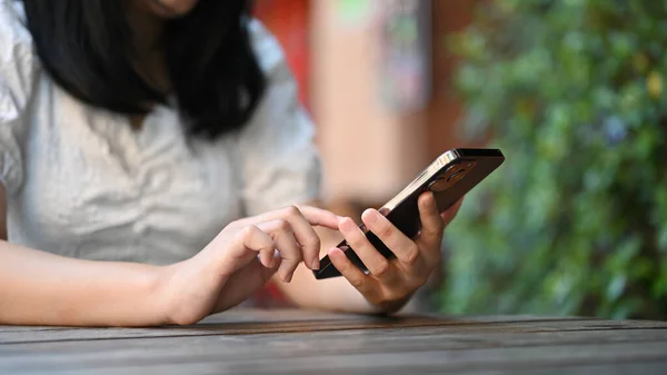 stock image cropped shot, Young Asian female using her smartphone while sitting a the outdoor coffee shop.