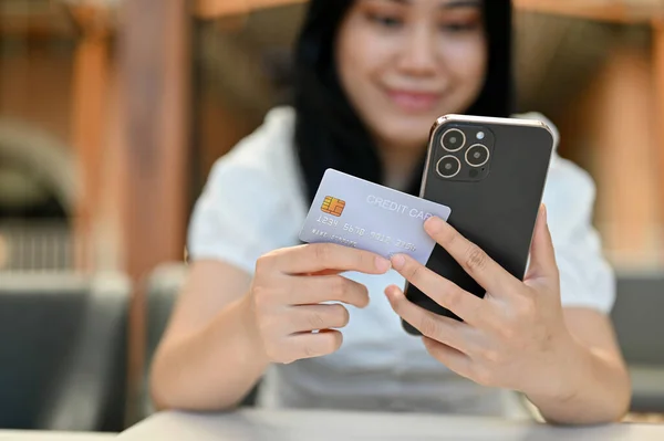 stock image Attractive young Asian woman holding a credit card and smartphone, using mobile banking to pay online bills. cropped image