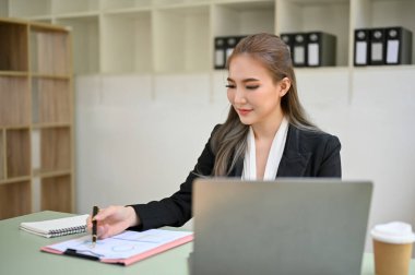 Ofisinde çalışan çekici Asyalı iş kadını ya da bayan yönetici, iş raporlarını kontrol ediyor ya da inceliyor..