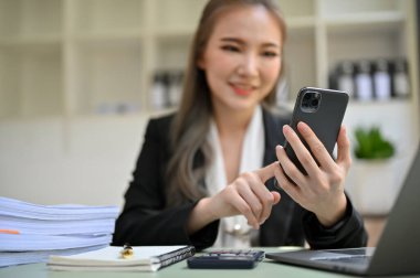 Güzel Asyalı iş kadını ya da kadın muhasebeci masasında otururken biriyle konuşmak için cep telefonunu kullanıyor..