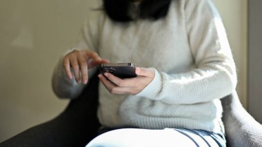 Günlük kıyafetlerle kafede oturan, akıllı telefonunu arkadaşlarıyla sohbet etmek için kullanan ya da sosyal medyasına kayan bir kadın. Teknoloji ve insan kavramı. Yakın çekim ve kırpılmış çekim