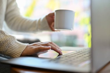 Kahve dükkanında çalışan, kahvesini yudumlarken dizüstü bilgisayar kullanan serbest çalışan bir kadın. kırpılmış resim