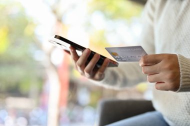 Kafede otururken elinde kredi kartı ve akıllı telefonu olan Asyalı bir kadın. kırpılmış resim