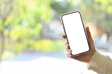 Akıllı telefon beyaz ekran modeli arka planda bulanık bir dış görünüm üzerinde bir kadının elinde..