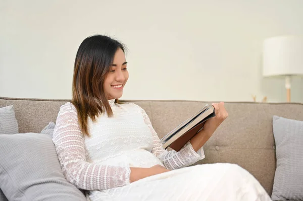 当年轻的亚洲孕妇在客厅休息的时候 她在看书 这让她松了口气 母亲和生活方式概念 — 图库照片
