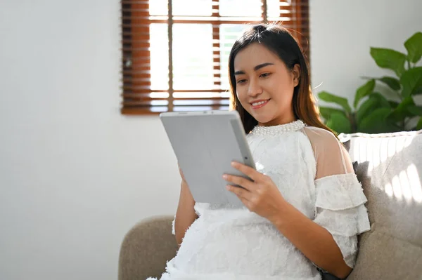 在客厅休息的时候 快乐迷人的亚洲孕妇正在平板电脑上观看网上的新生儿护理视频 母性概念 — 图库照片