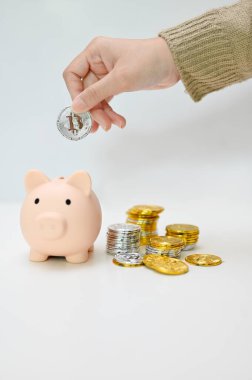 Bir kadın kumbara içine bozuk para yerleştiriyor. Beyaz arka planda altın ve gümüş para yığını. Para biriktirme kavramı