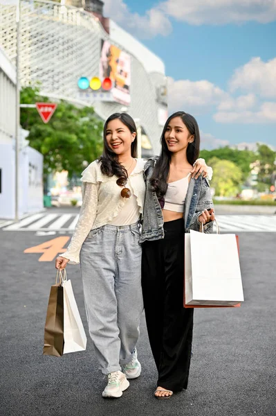 Two attractive young Asian women walking on the street with their shopping bags, enjoy shopping on the weekend together. Urban lifestyle concept