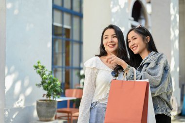 Çekici genç Asyalı kadın elbise dükkanını işaret ediyor, arkadaşlarıyla alışveriş caddesinde alışveriş yapmaktan hoşlanıyor. Kentsel yaşam tarzı konsepti