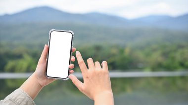 Genç Asyalı kadın göl ve dağın fotoğrafını çekmek için modern akıllı telefonunu kullanıyor. Telefon beyaz ekran modeli. Seyahat ve teknoloji konsepti