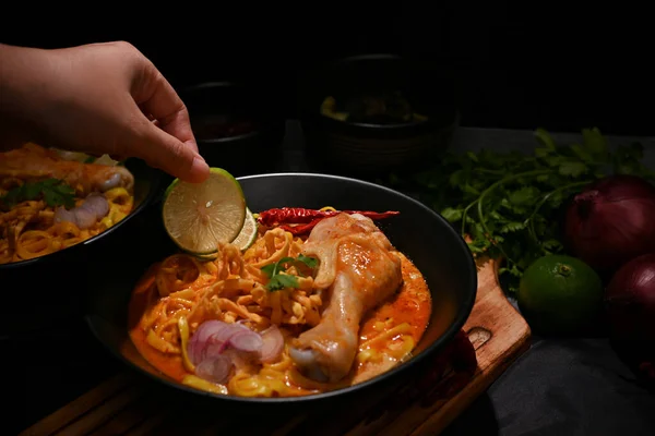 stock image A female chef garnishing her Khao Soi Kai with a lime slide, Khao Soi Kai or Thai noodles curry with egg noodles and chicken drumstick.