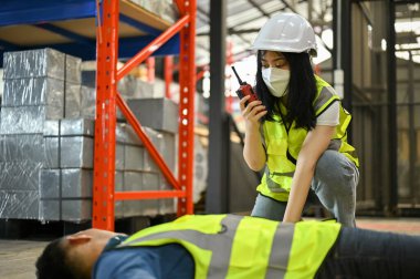 Telsiz kullanan kadın bir depo çalışanı baygın bir adamı kurtarmak için fabrikanın ilk yardım ekibini aramış. işyeri kazası kavramı